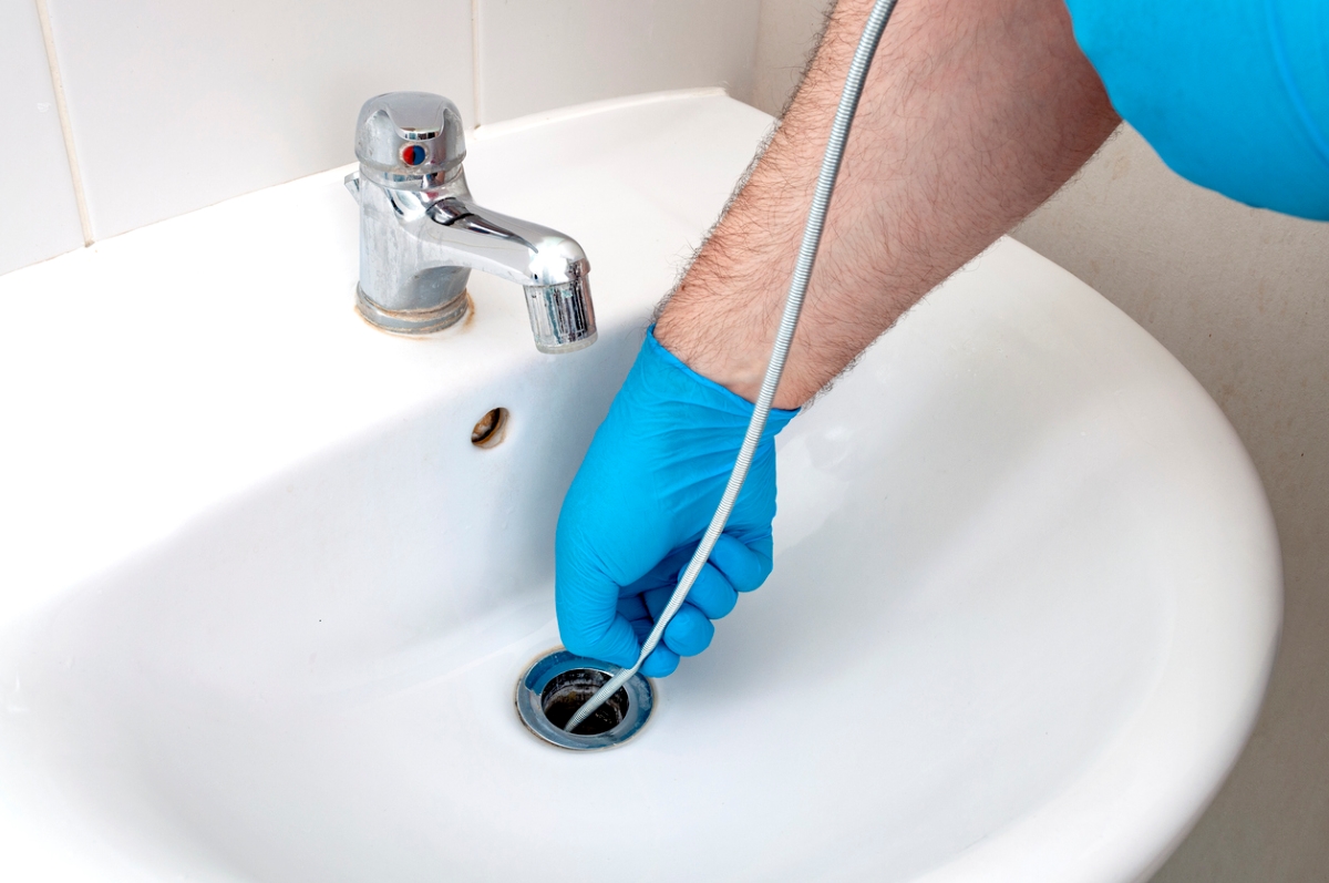 Person pushing snake in drain to unclog sink