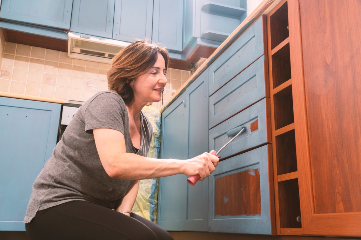 Woman using roller to paint laminate cabinets teal blue.