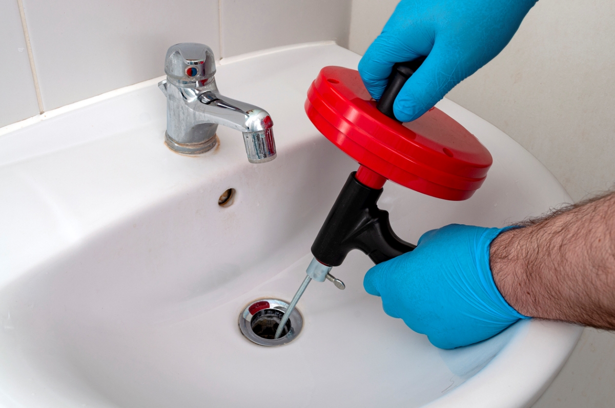 Gloved hands using drain auger in sink