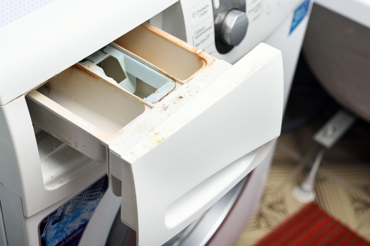 A front-loading washing machine's dispenser tray is open and is dirty.