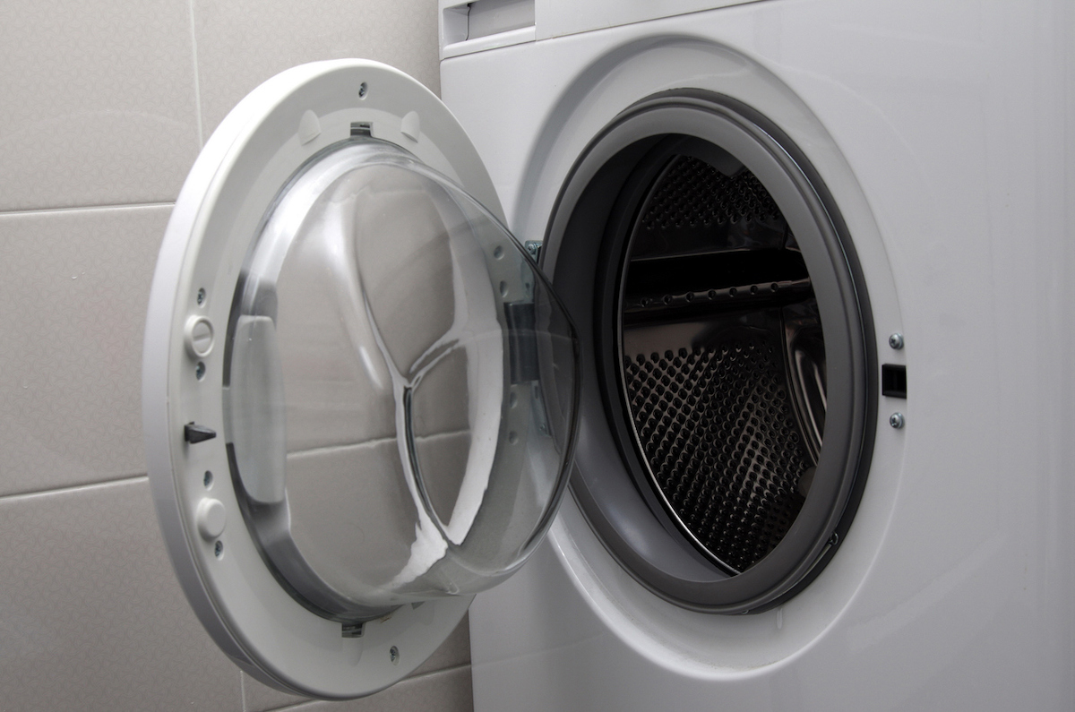 An empty front-loader washing machine's door is open in a white tiled room.