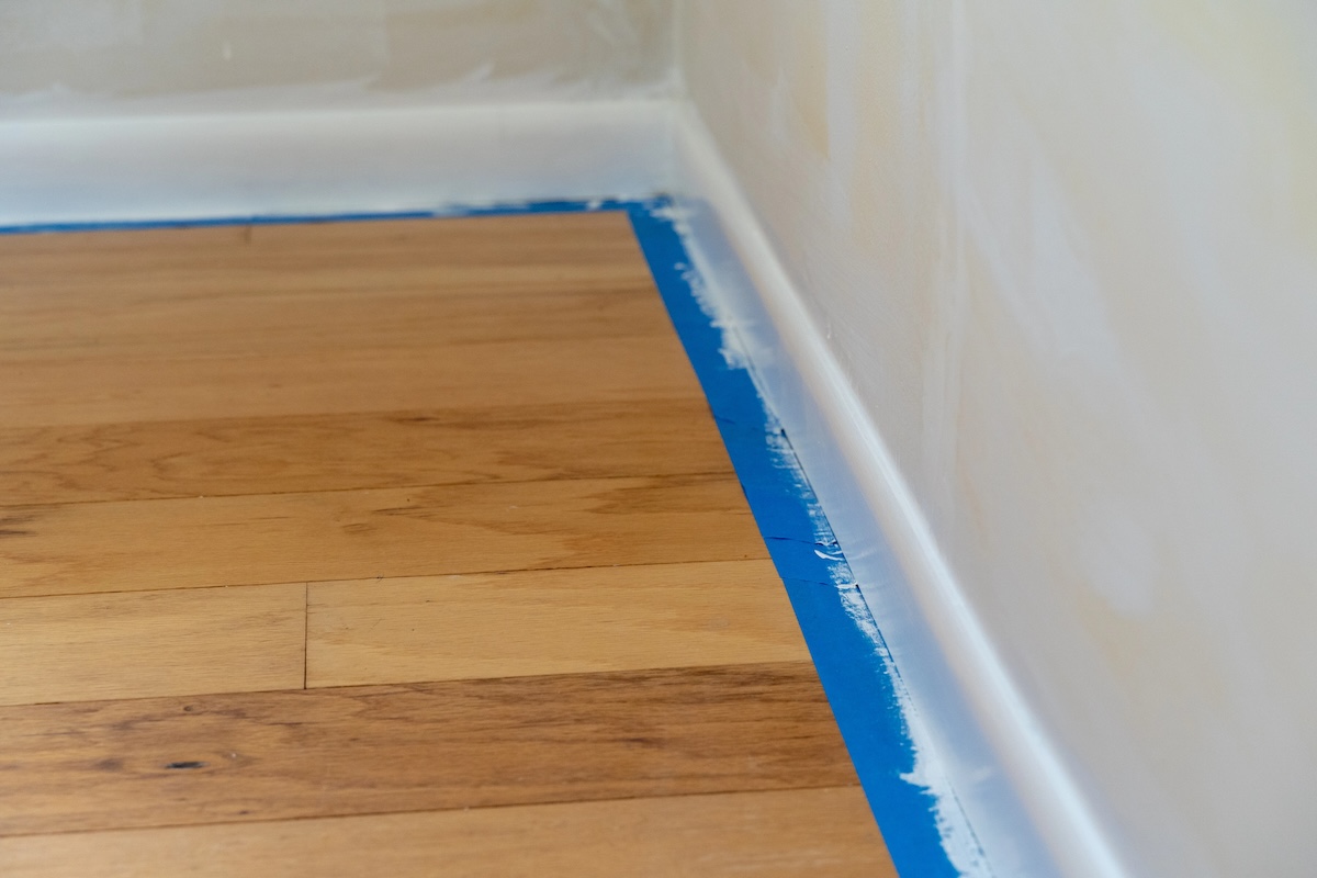 Blue painters tape on house baseboards being painted.