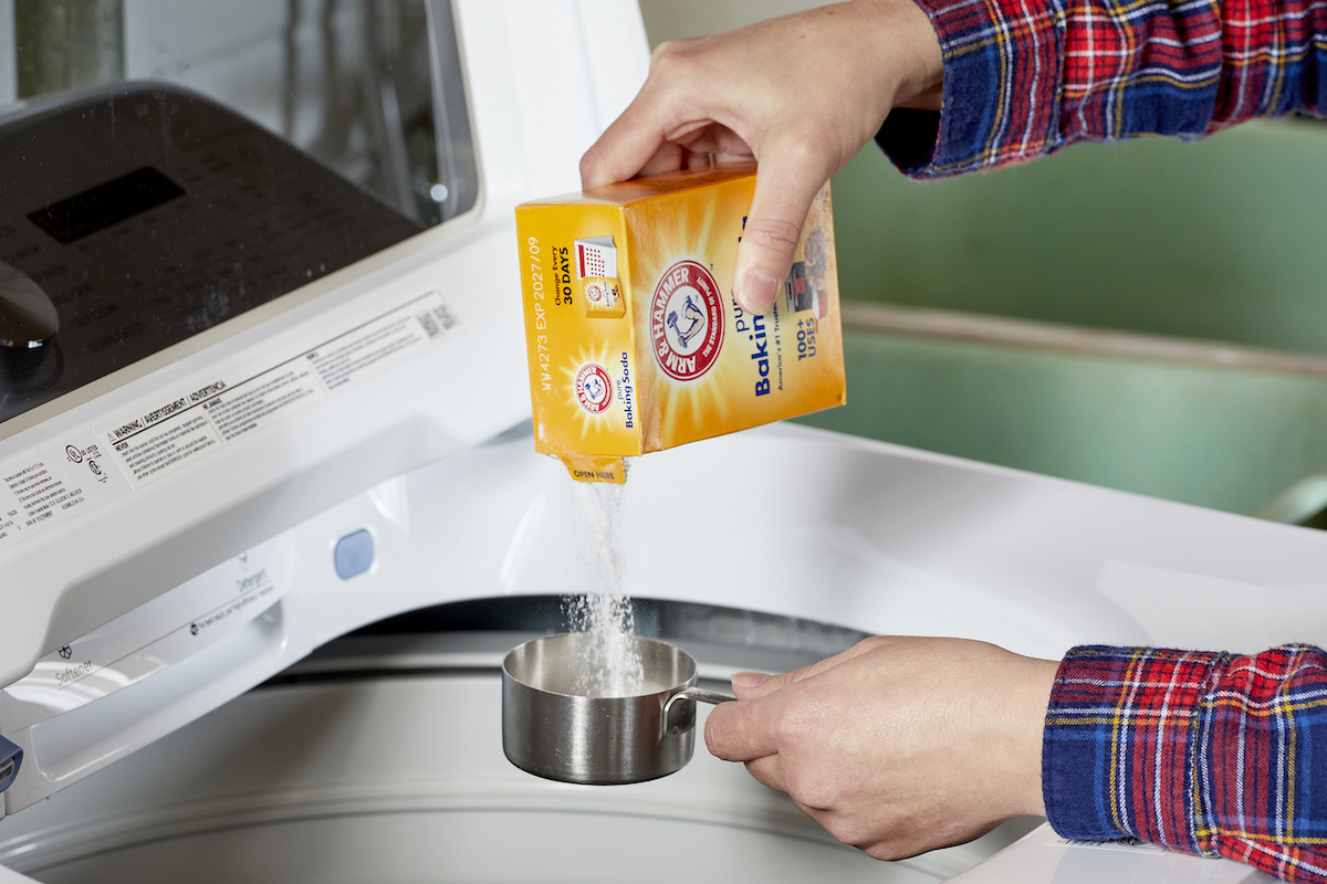 Woman measures baking soda into a measuring cup over a top-load washing machine.