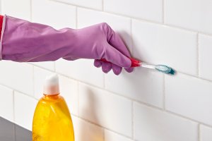 Woman uses toothbrush to apply homemade grout cleaner to tile grout.