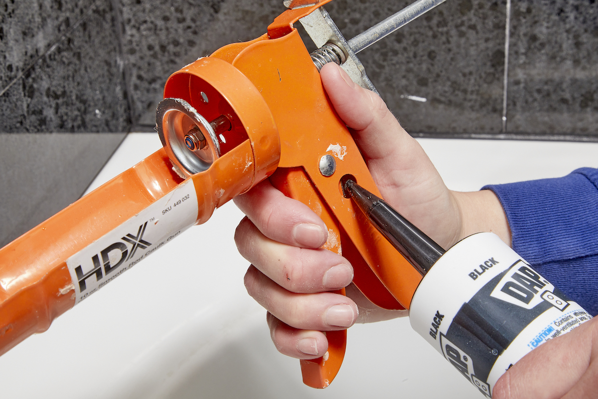Woman cuts tip on caulk on the joint of a caulking gun.
