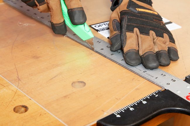 Person running knife against ruler on thin plexiglass.