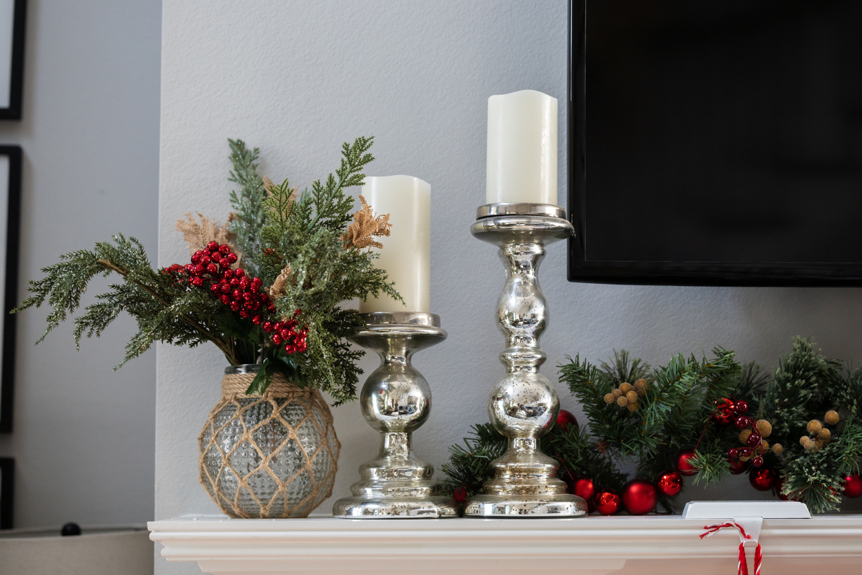 A decorated white Christmas mantle with pine garland, silver candleholders with candles and a television.