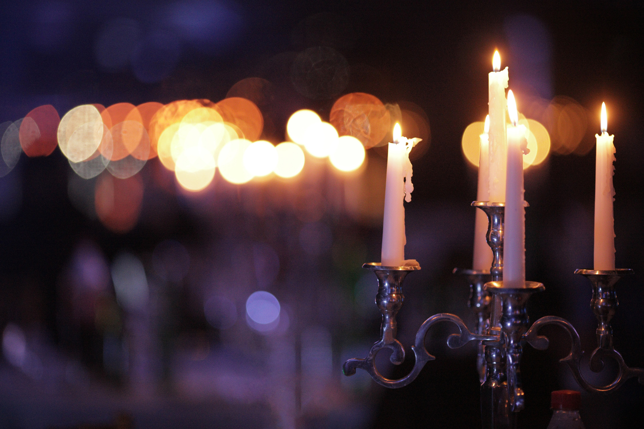 Metal retro candlestick with five burning candles against a dark background in the room