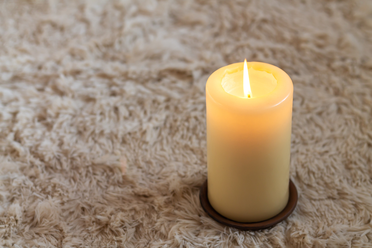 Cozy large burning candle on carpet.