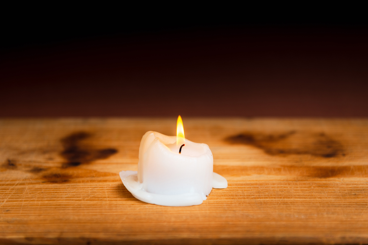 a single lit candle on a wood surface.