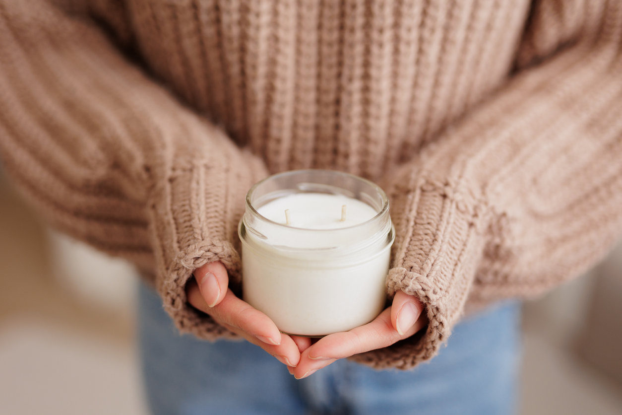 Woman in brown sweater holding finished white candle in hands