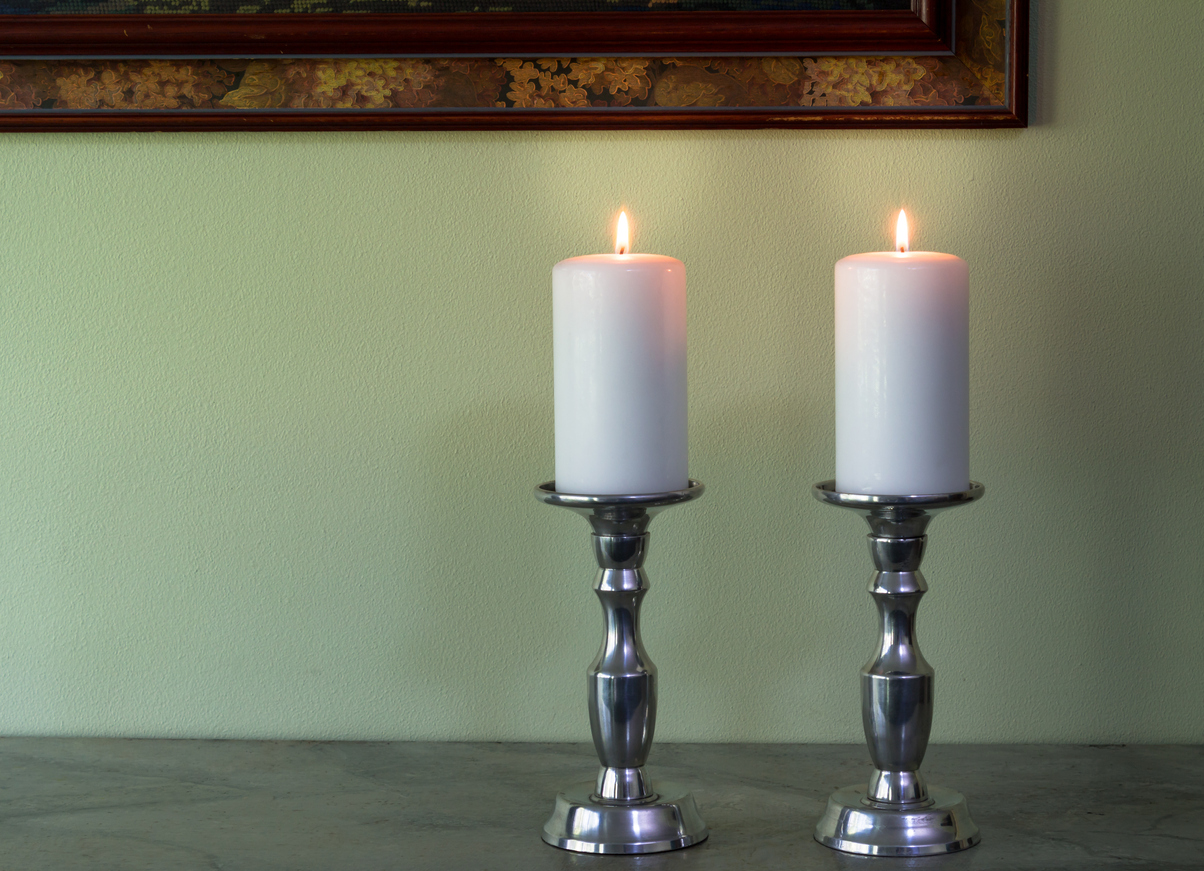 Two lit white candles in canelabra against green wall texture background