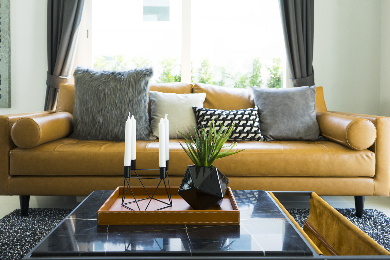 Brown leather sofa near a coffee table with black vase and modern candle holder.