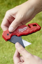 Person holding Milwaukee Fastback utility knife open with green grass in the background.