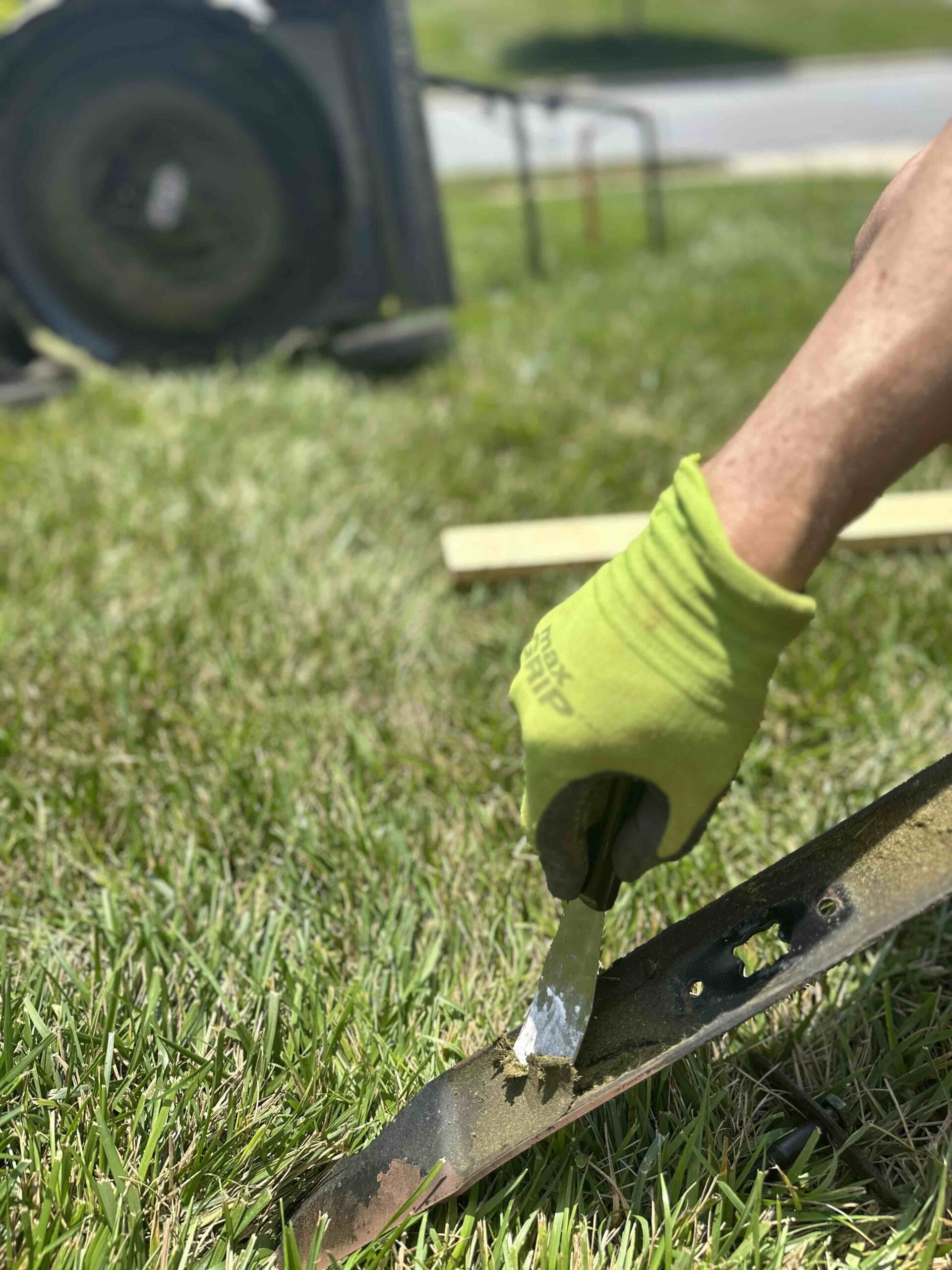 Close up of man's hand's in green gardening gloves sharpening lawn mower blade