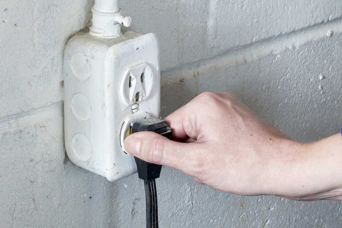 Woman unplugs her clothes dryer from the electrical outlet.
