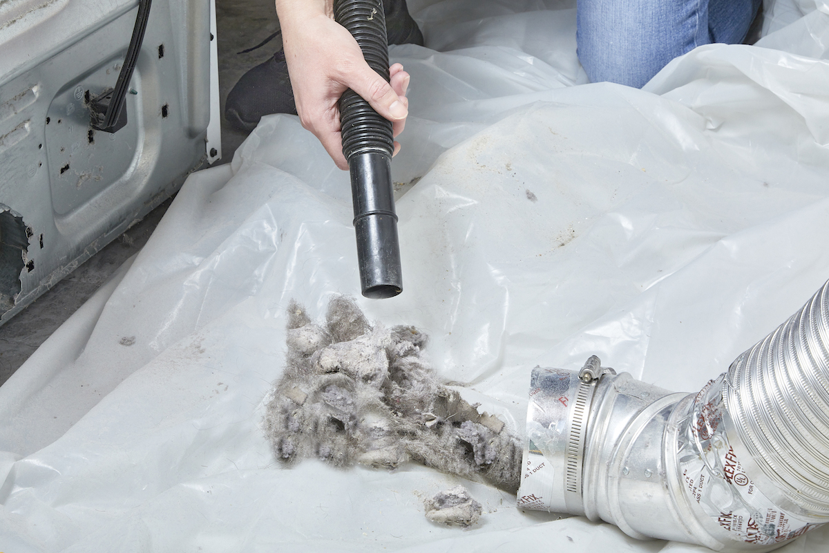 Dryer vent hose on top of a plastic drop cloth, with woman using shop vac to vacuum debris.