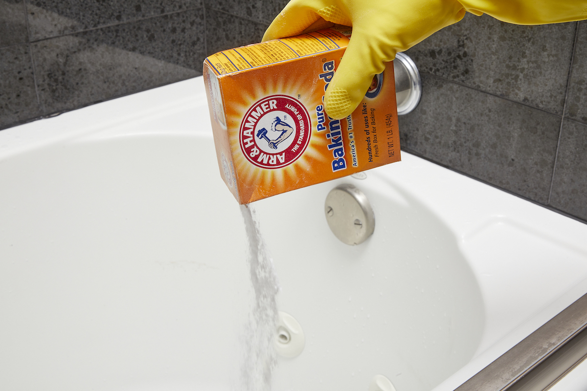 Woman pours baking soda from box into jetted tub.