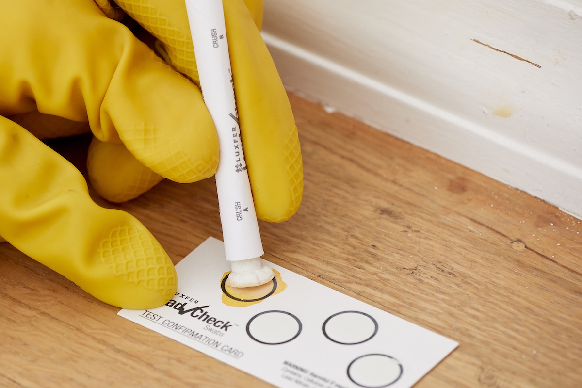 Person wearing yellow rubber gloves applies lead test swab to testing card.