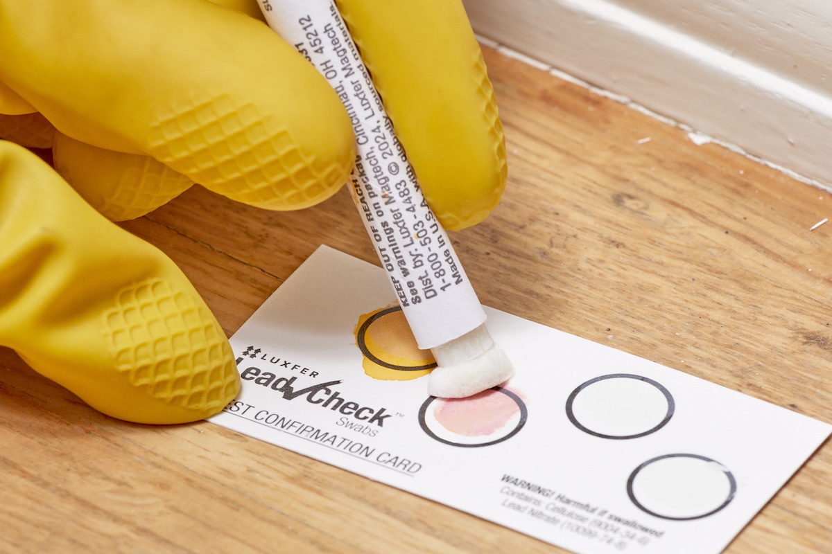 Person wearing yellow rubber gloves presses lead testing swab into second circle of testing card.