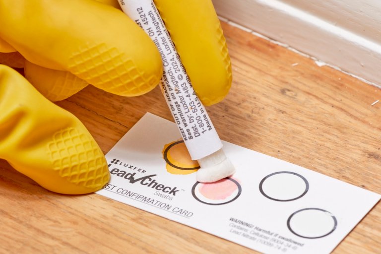 Person wearing yellow rubber gloves presses lead testing swab into second circle of testing card.