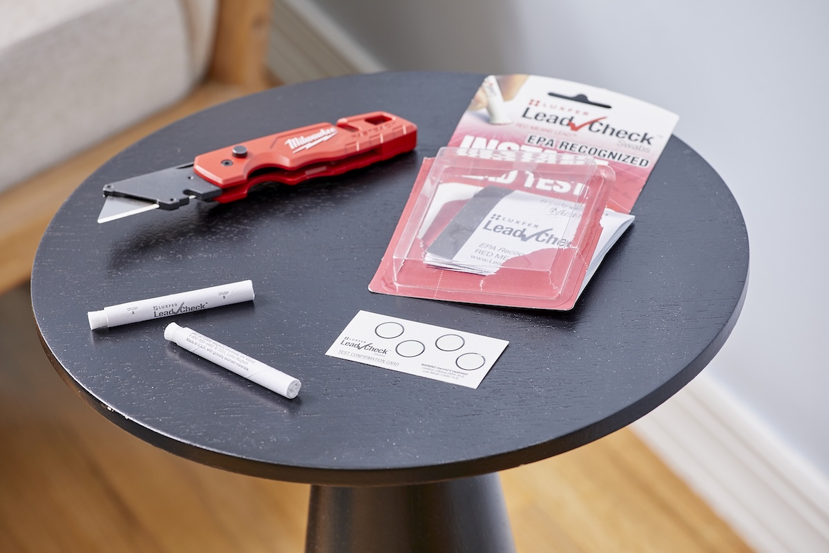 A lead paint testing kit and a utility knife are displayed on a small black round table.