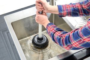 Woman uses plunger to clear a sink drain.