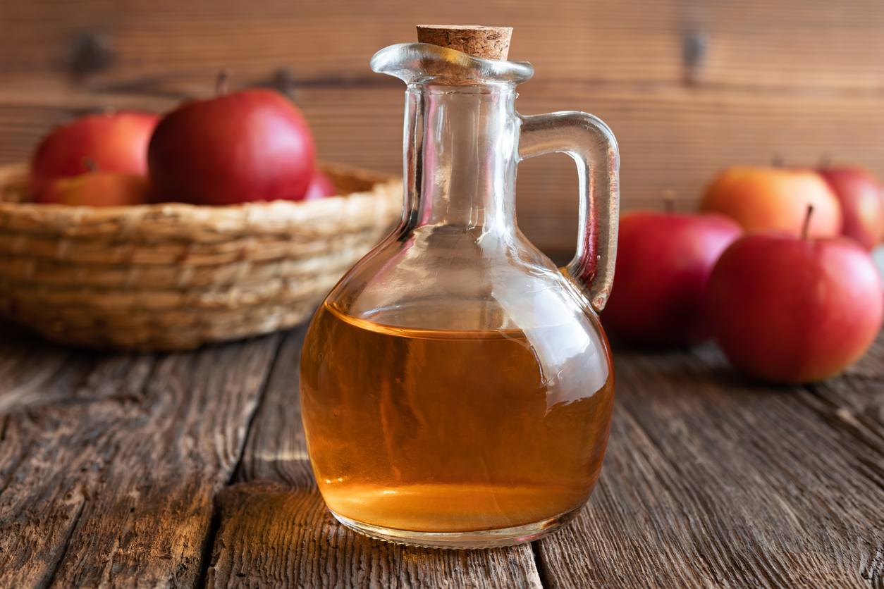 A bottle of apple cider vinegar with fresh apples in the background