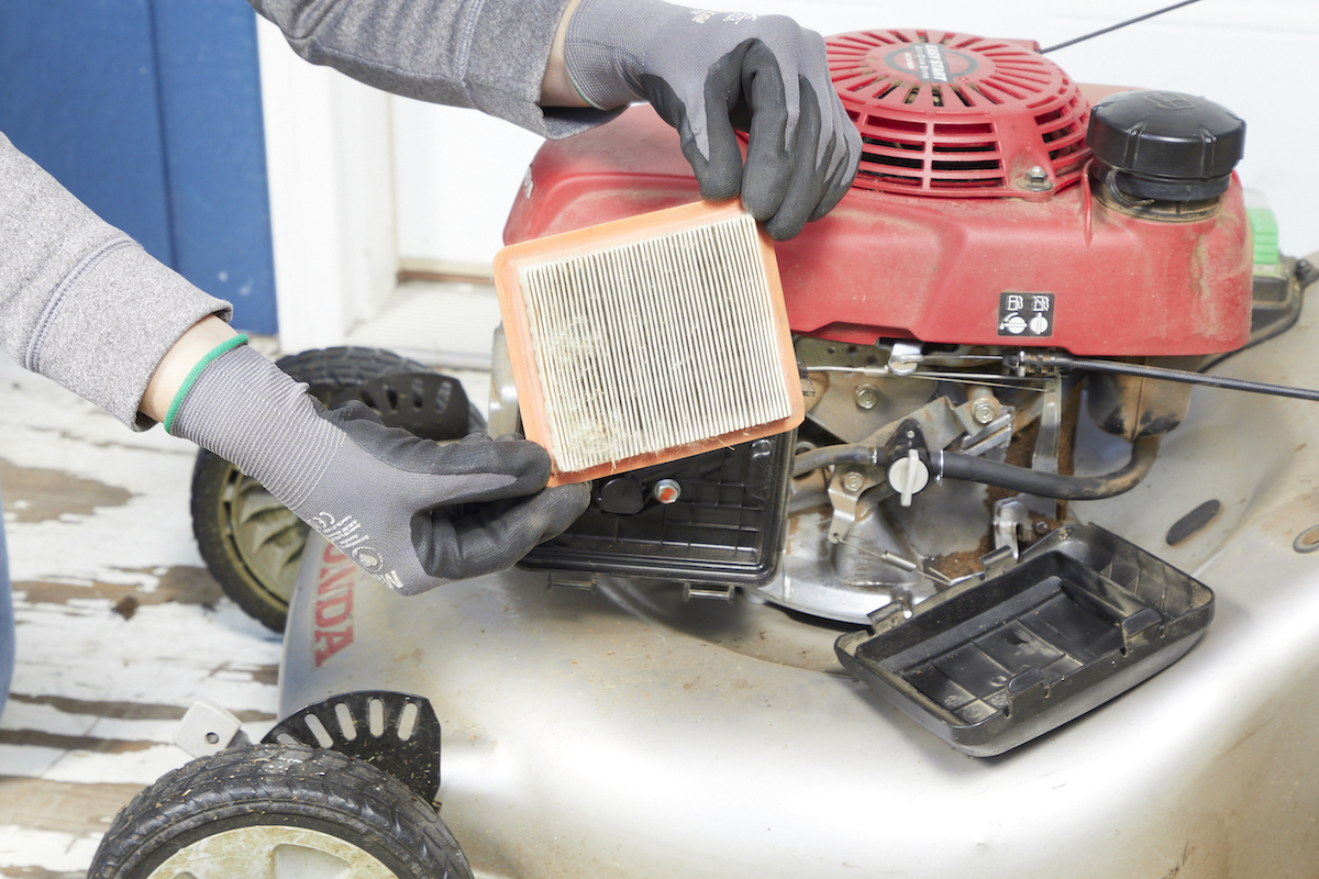 Woman wearing work gloves removes the filter from a lawn mower.