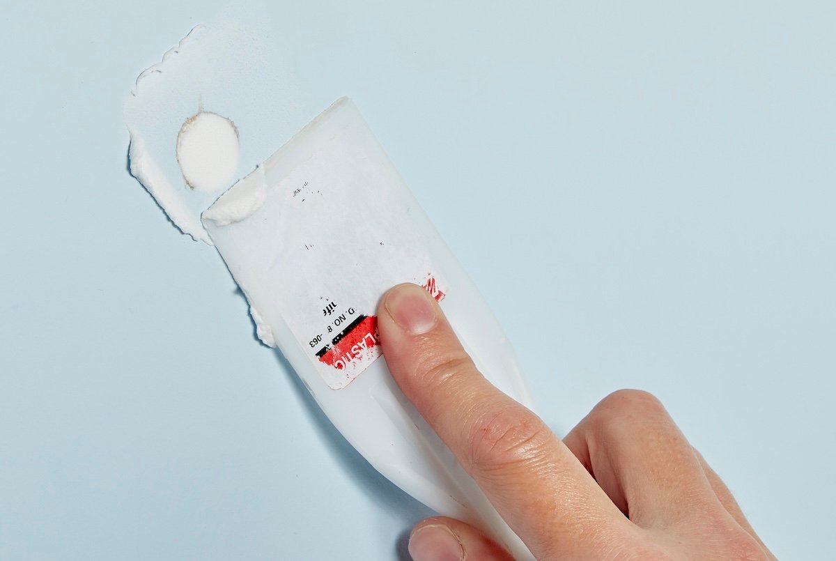 Person uses plastic putty knife to fill hole in drywall with joint compound.