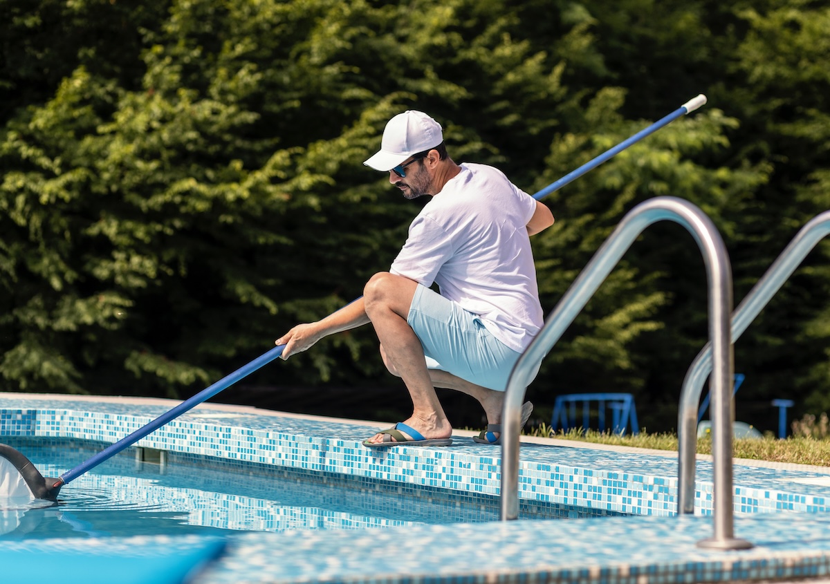 Man in flip flops cleaning the swimming pool with a net.