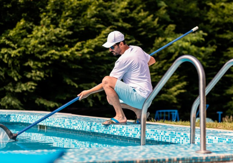 Man in flip flops cleaning the swimming pool with a net.