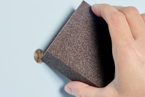 Woman uses a sanding block to clean a hole in drywall.