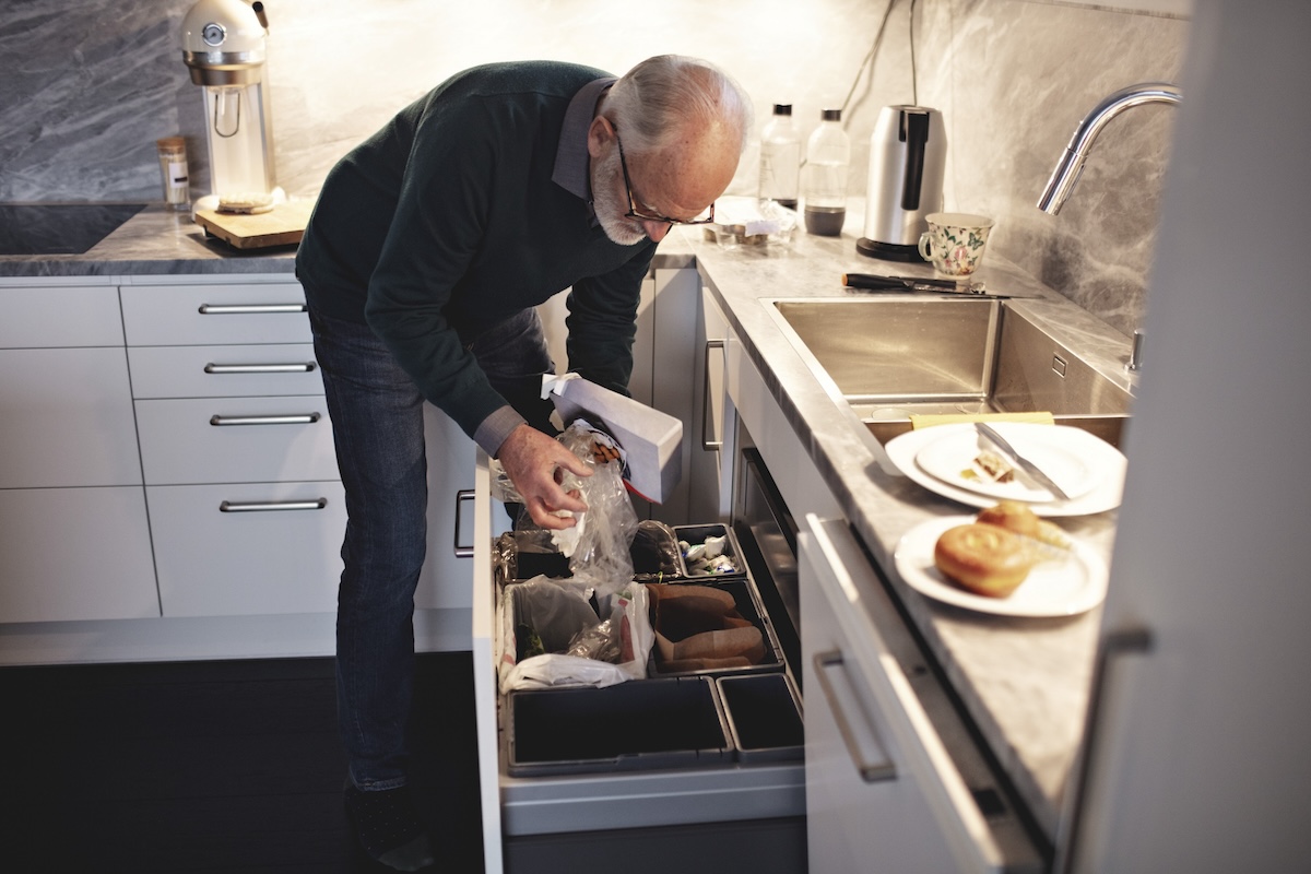 A mature gentleman throws away boxes of food in the trash.