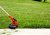 Red lawn edger runs along a driveway cutting grass beyond the driveway.