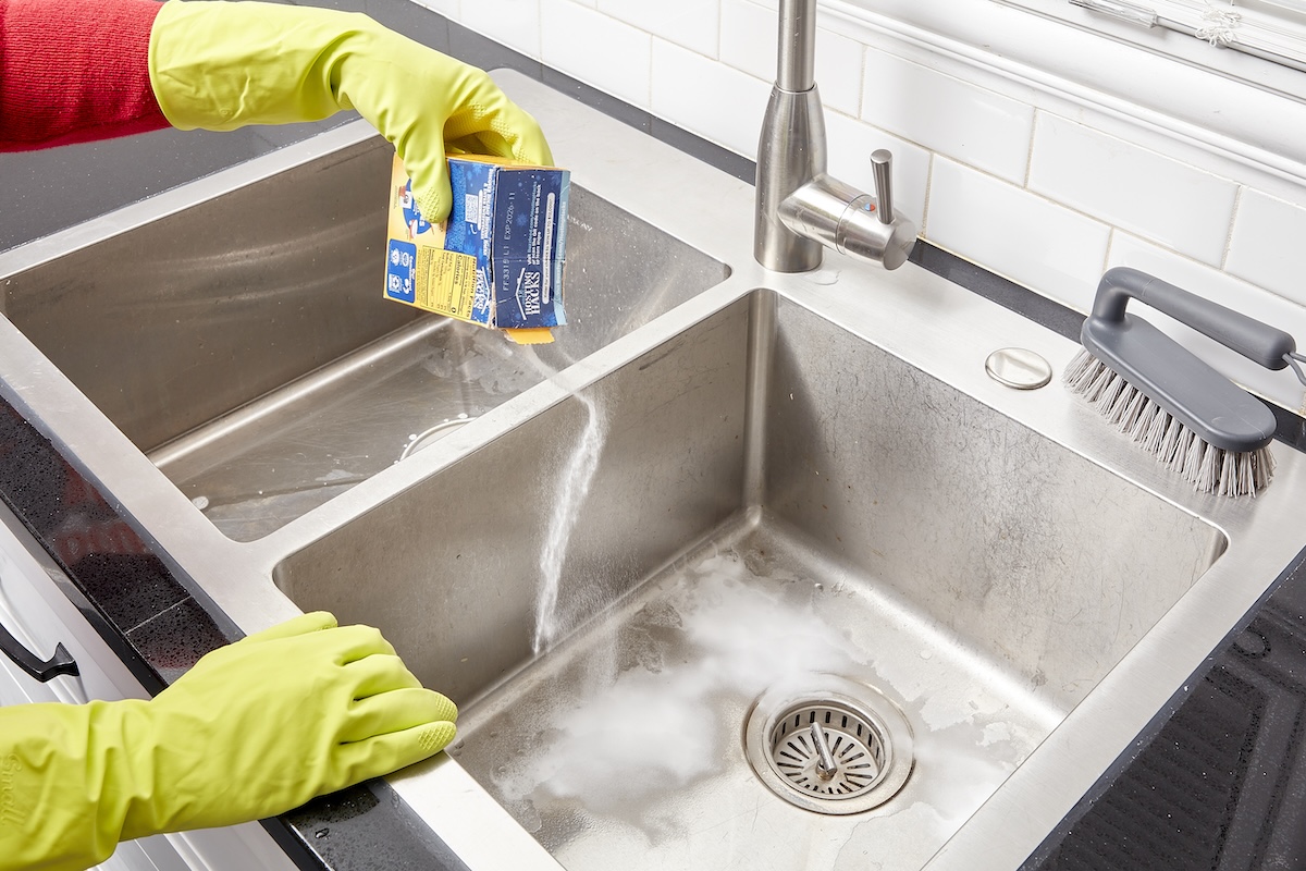Sprinkling baking soda on a stainless steel sink to clean it. 
