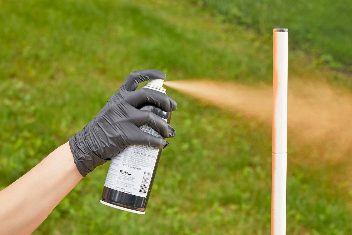Woman spray paints the metal leg of a table.