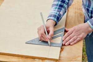 Person uses a speed square to draw a straight line on a wood board.