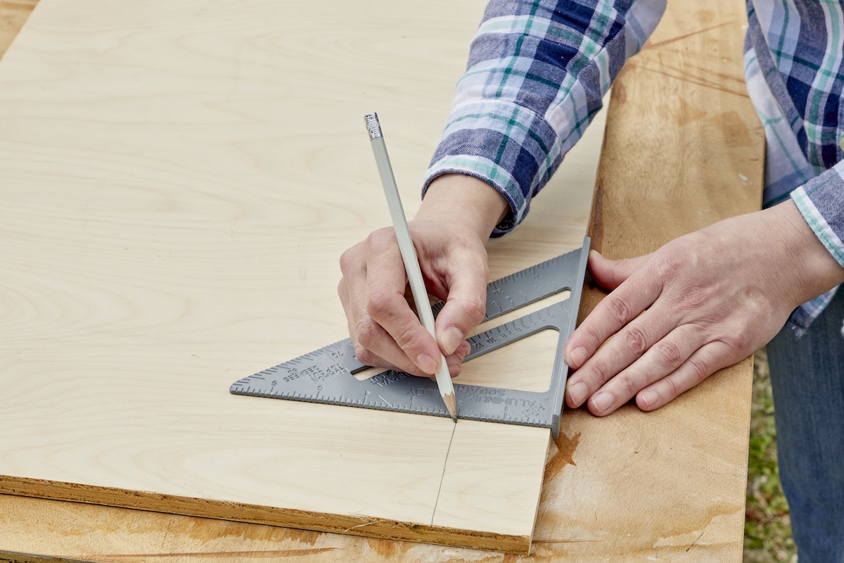 Person uses a speed square to draw a straight line on a wood board.
