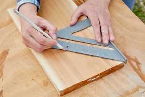 Person draws a line across the hypotenuse of a speed square onto a wood board.