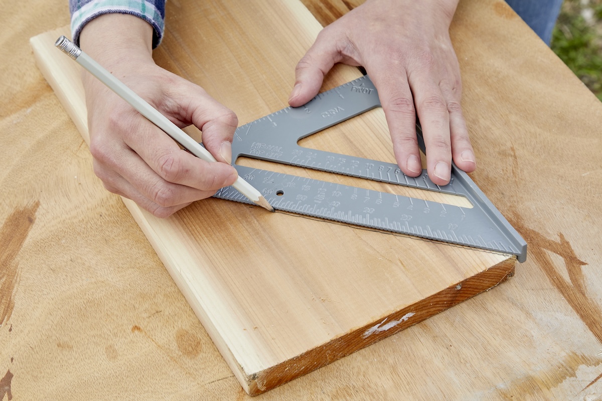 Person draws a line across the hypotenuse of a speed square onto a wood board.