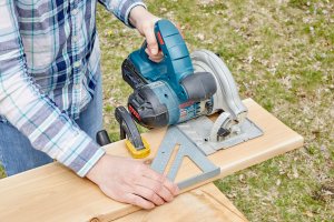 Woman uses a speed square for a saw guide at an outdoor workbench.