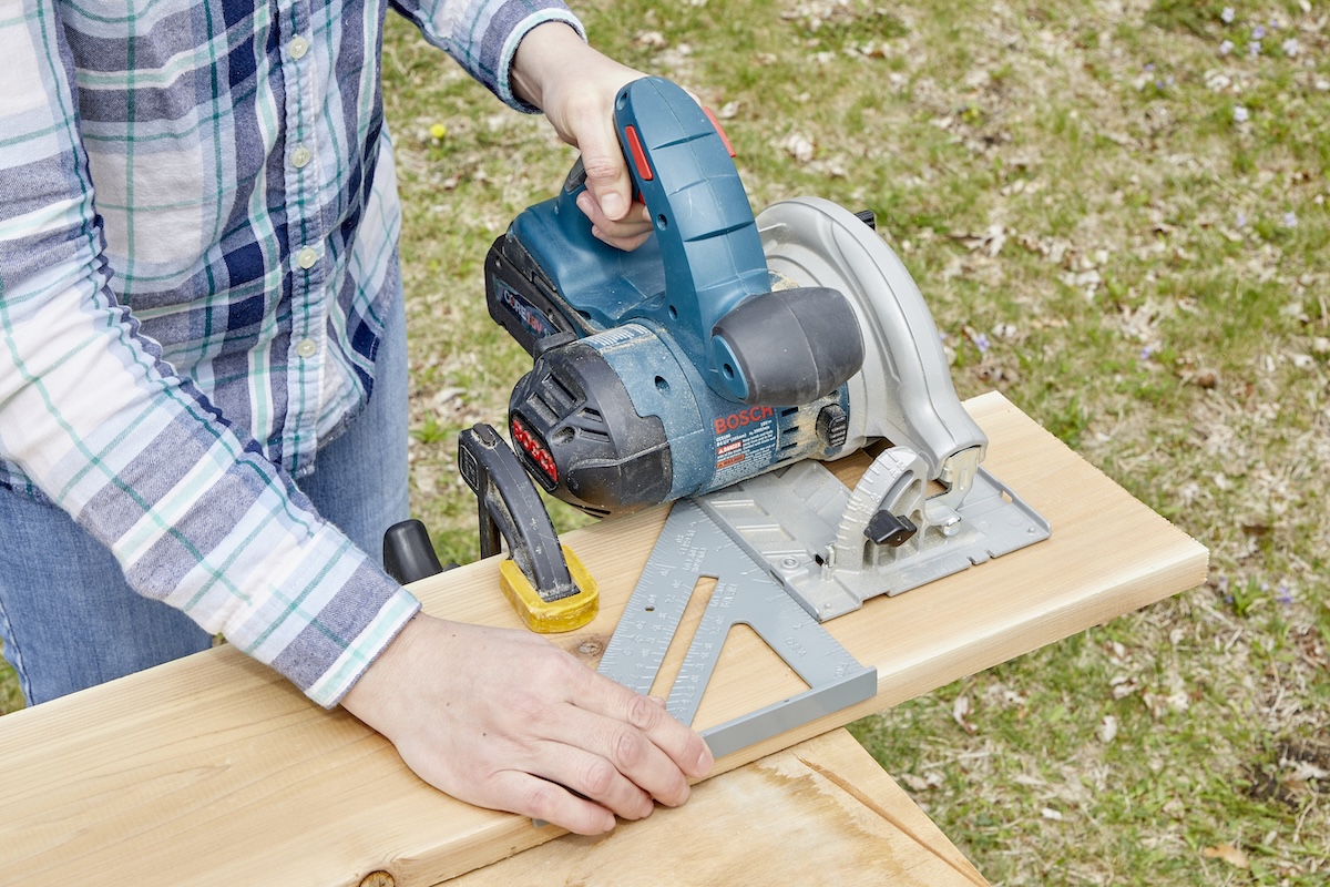Woman uses a speed square for a saw guide at an outdoor workbench.