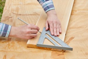 Person uses a speed square to draw a straight line on a wood board.