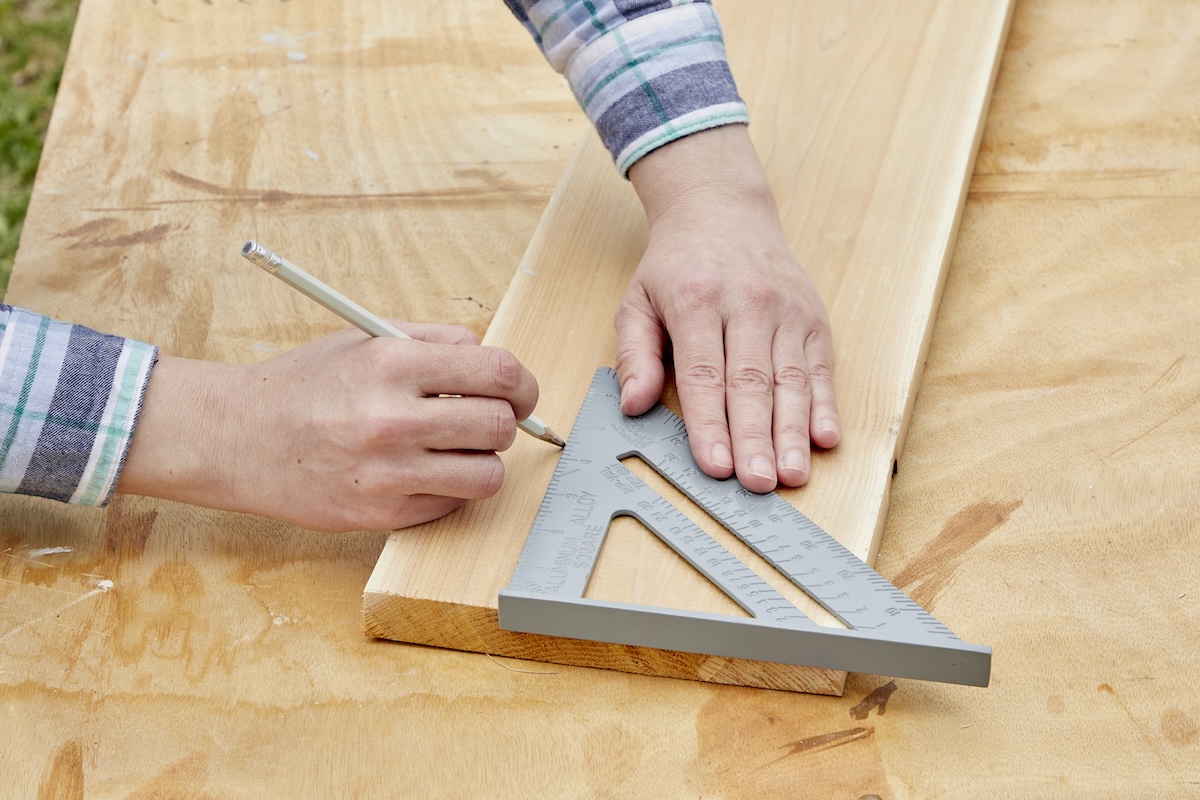 Person uses a speed square to draw a straight line on a wood board.