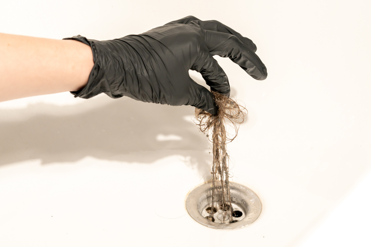 Person with black rubber glove cleans hair from shower drain.