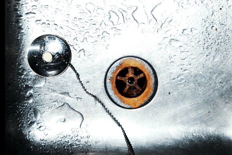 A stainless steel wash basin with rusty sink drain hole, plug hole and chain in sink.