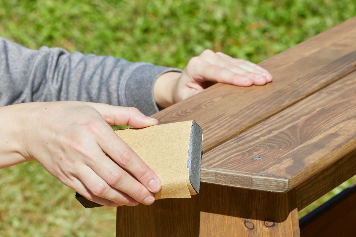 Woman uses a sanding block to sand a stained bench.