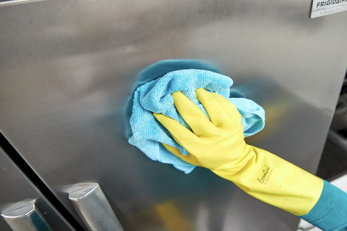 Wiping a stainless steel fridge with vinegar and a rag.