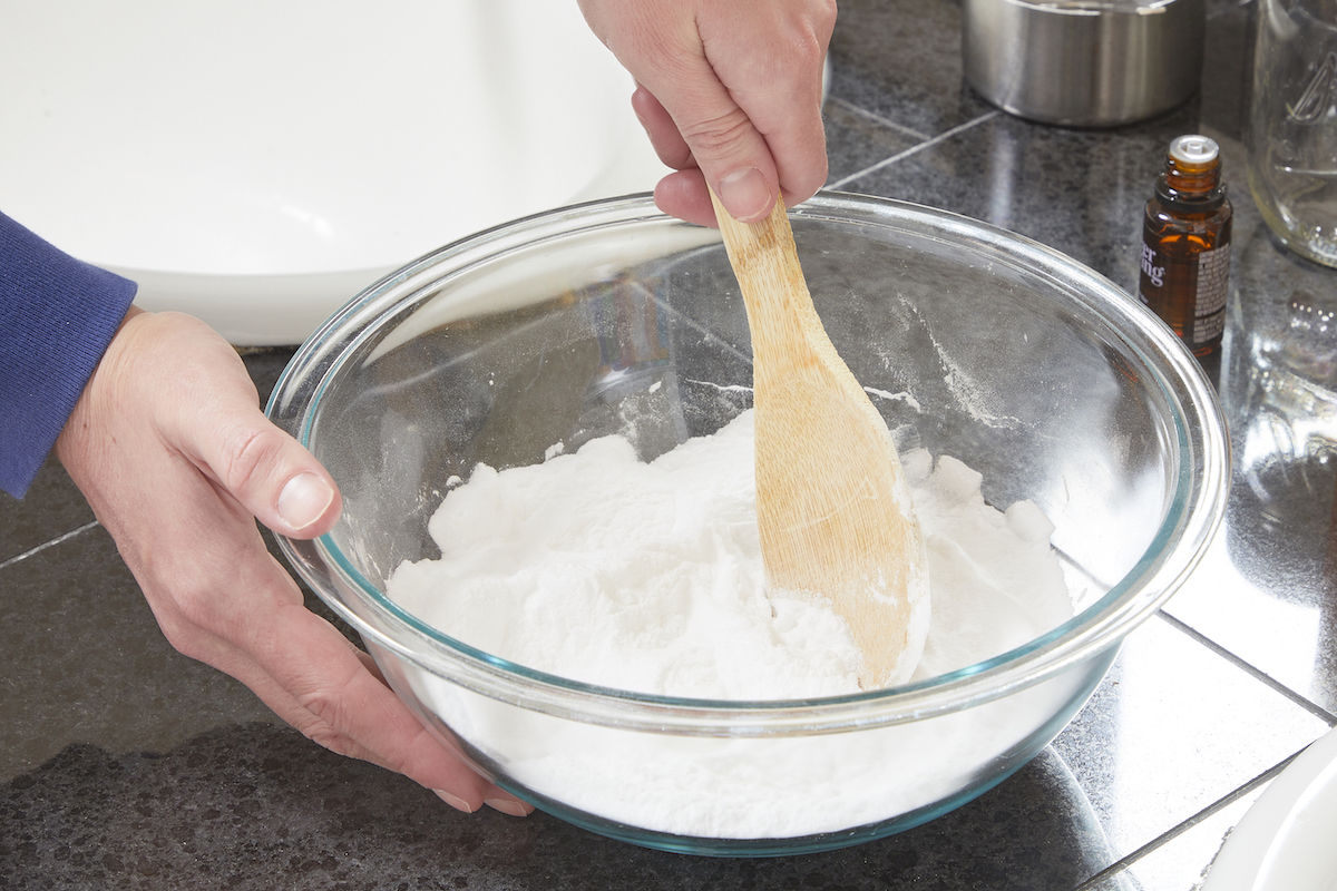 Woman using a wooden spoon to mix essential oils and baking soda.